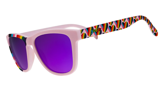 goodr We're Here to Slay. Exklusiva Pride-solglasögon från goodr med stilrena lavenderlila bågar med hjärtan i regnbågsfärger längst med bågarna och en regnbågsflagga över ena bågen